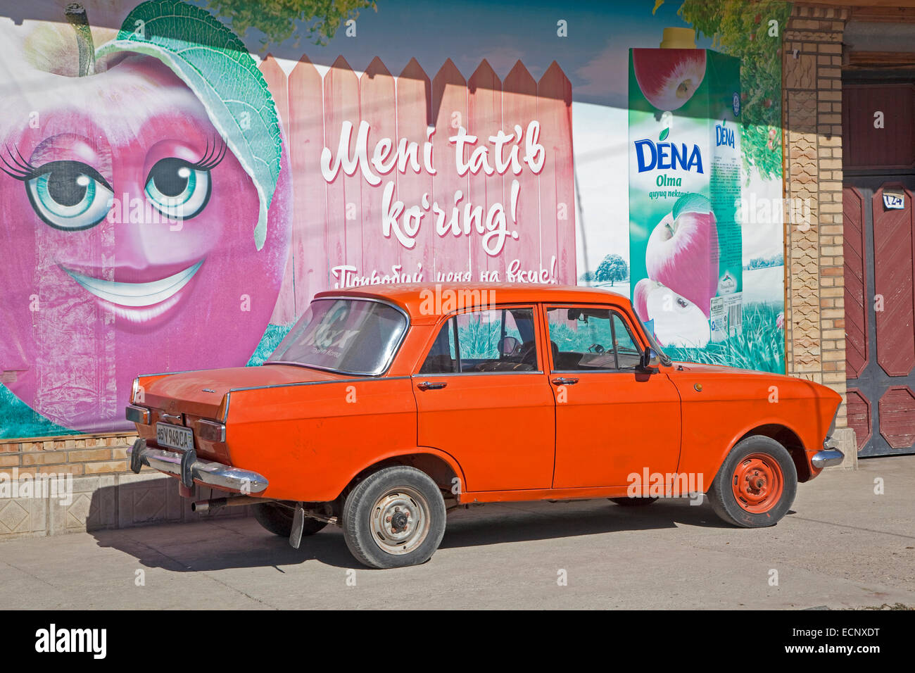 Vieille Trabant orange garé en face de la publicité peinte sur mur en Ouzbékistan Banque D'Images