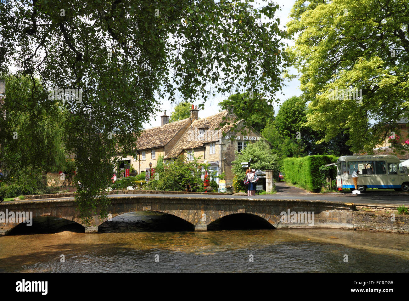 Un bas-arquée pont de pierre sur un ruisseau avec cottages en pierre de Cotswold sous des arbres. Banque D'Images