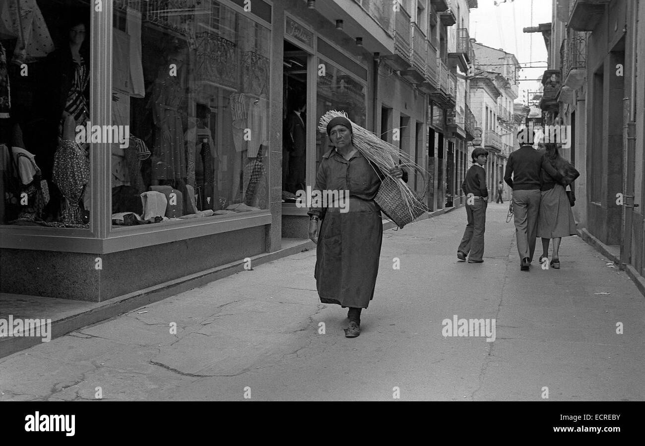 Une paysanne, habillé humblement, un chargement de paille sur ses épaules le long d'une rue de la ville. Le noir et blanc Banque D'Images