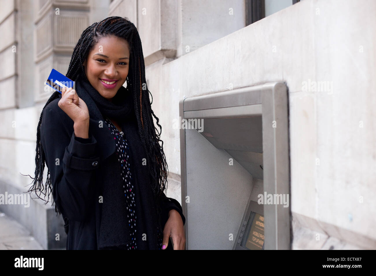 Une jeune femme tenant une carte de paiement à un distributeur mashine. Banque D'Images