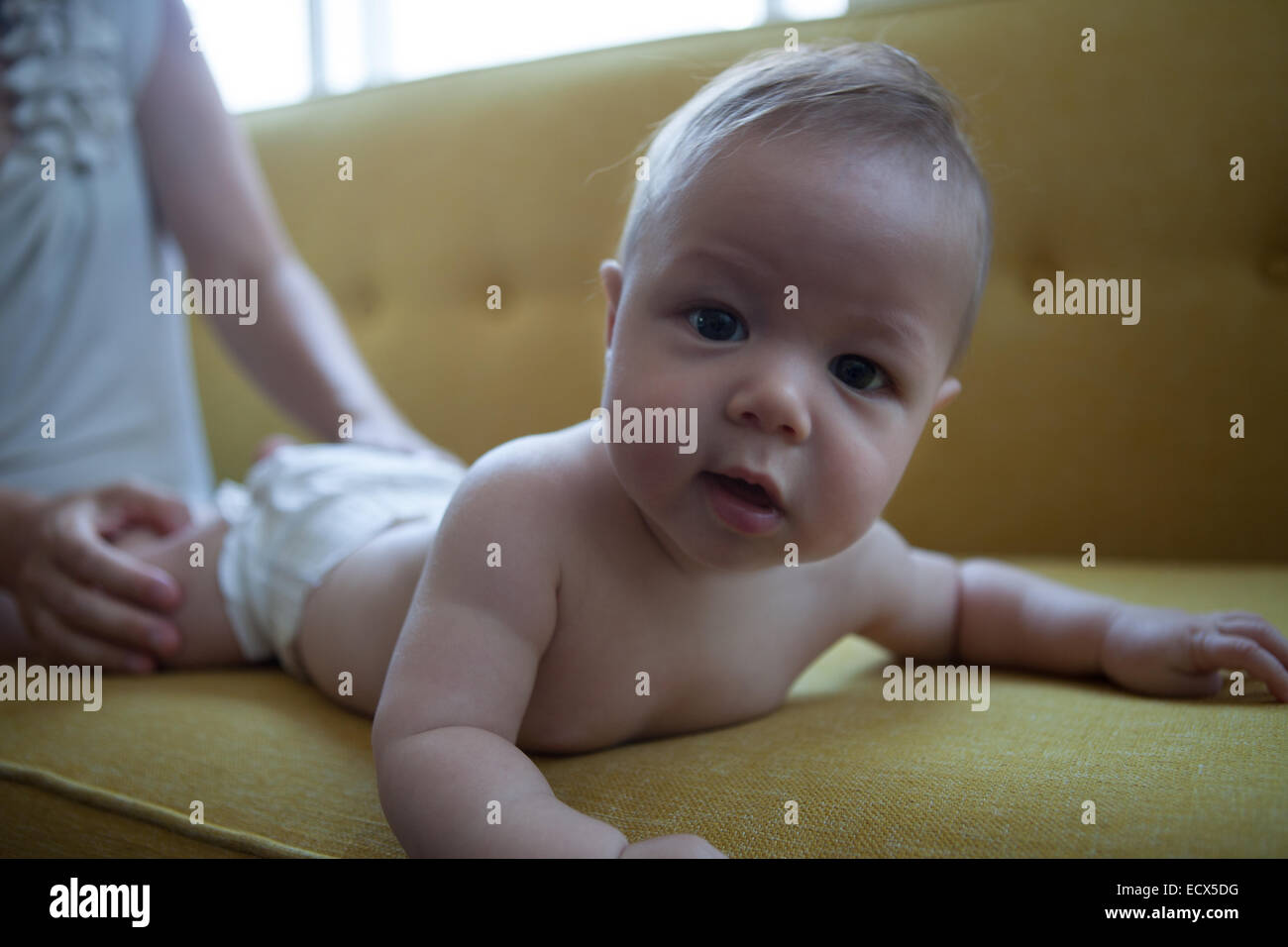 Portrait d'un petit bébé couché sur le canapé avant jaune, looking at camera Banque D'Images