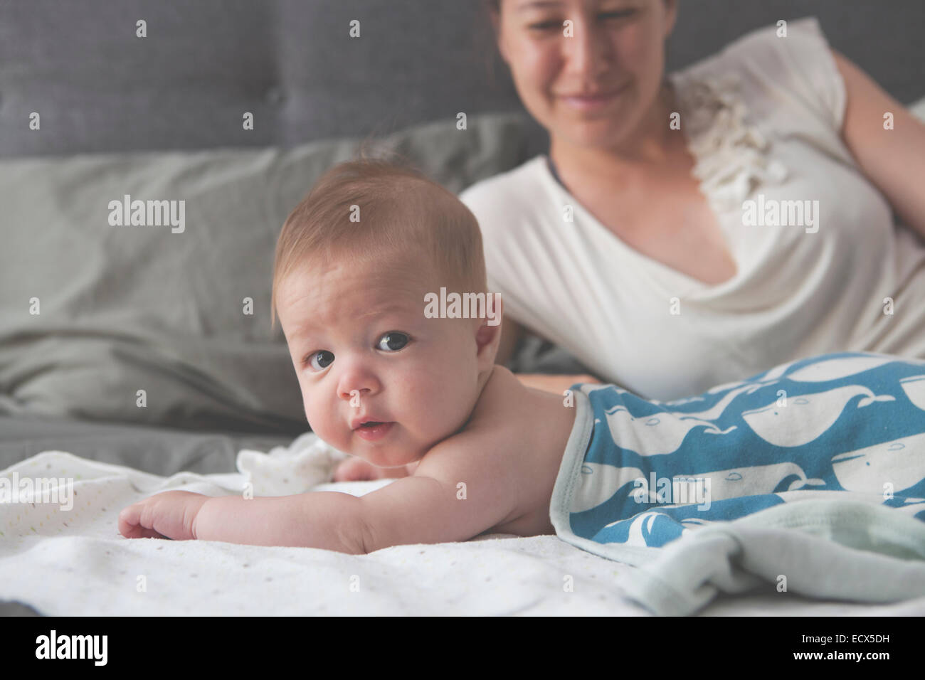 Portrait of little baby lying on bed with mother smiling in background Banque D'Images