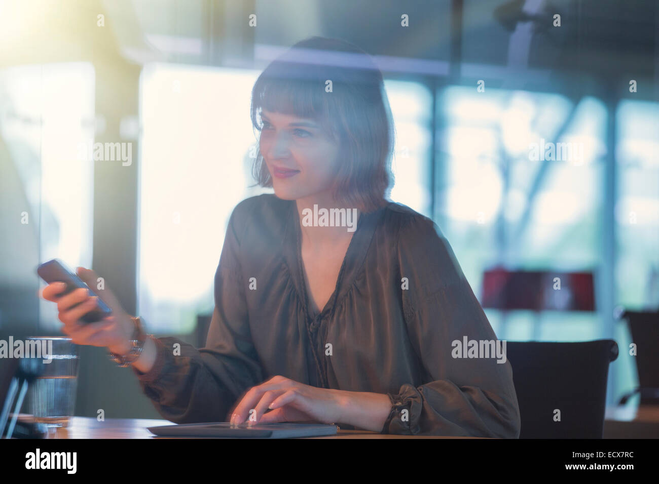 Businesswoman holding cell phone at office desk Banque D'Images