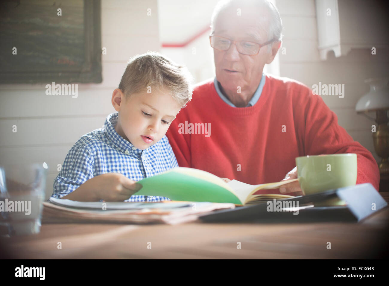 Boy reading avec grand-père à table Banque D'Images