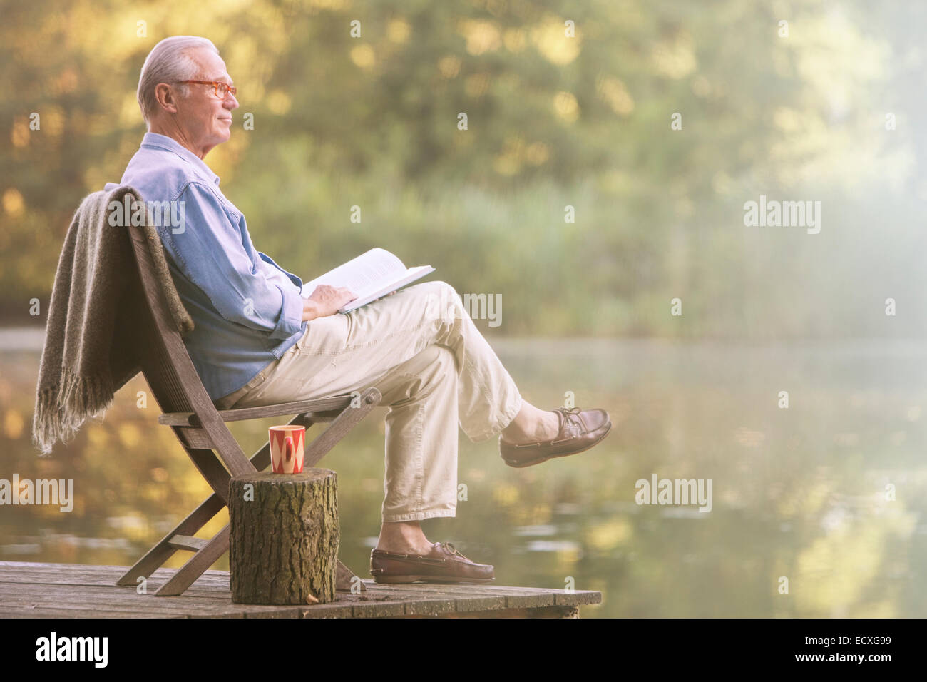 Older Man reading book on dock at Lake Banque D'Images