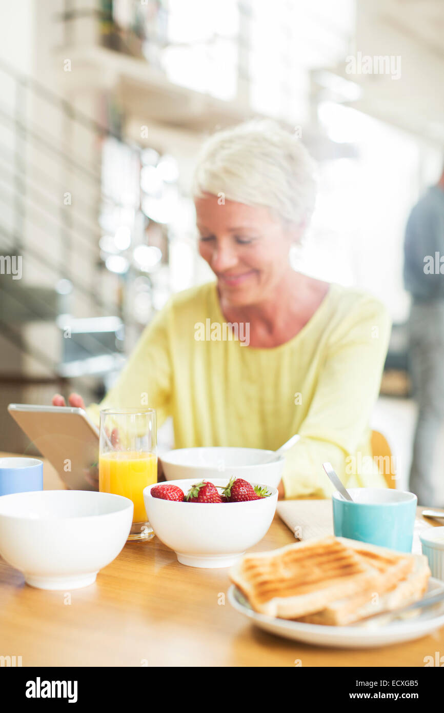 Plus woman using digital tablet at breakfast table Banque D'Images