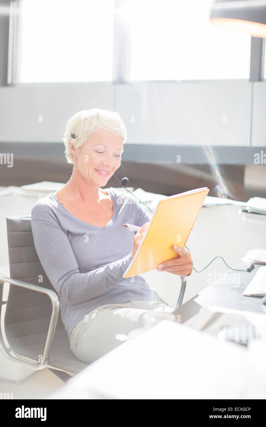 Young écrit dans l'ordinateur portable casque at office desk Banque D'Images