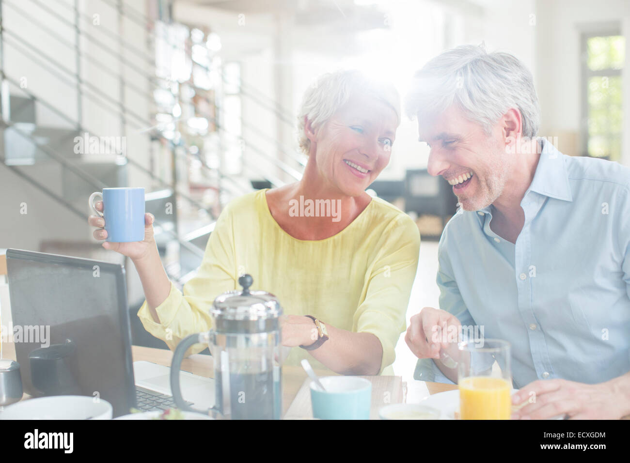 Vieux couple laughing at breakfast table with laptop Banque D'Images