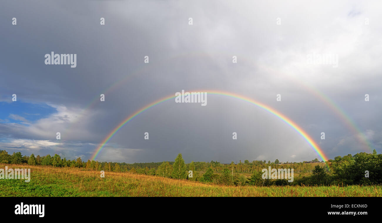 Un double arc-en-ciel lumineux sur arches un village champ. Banque D'Images