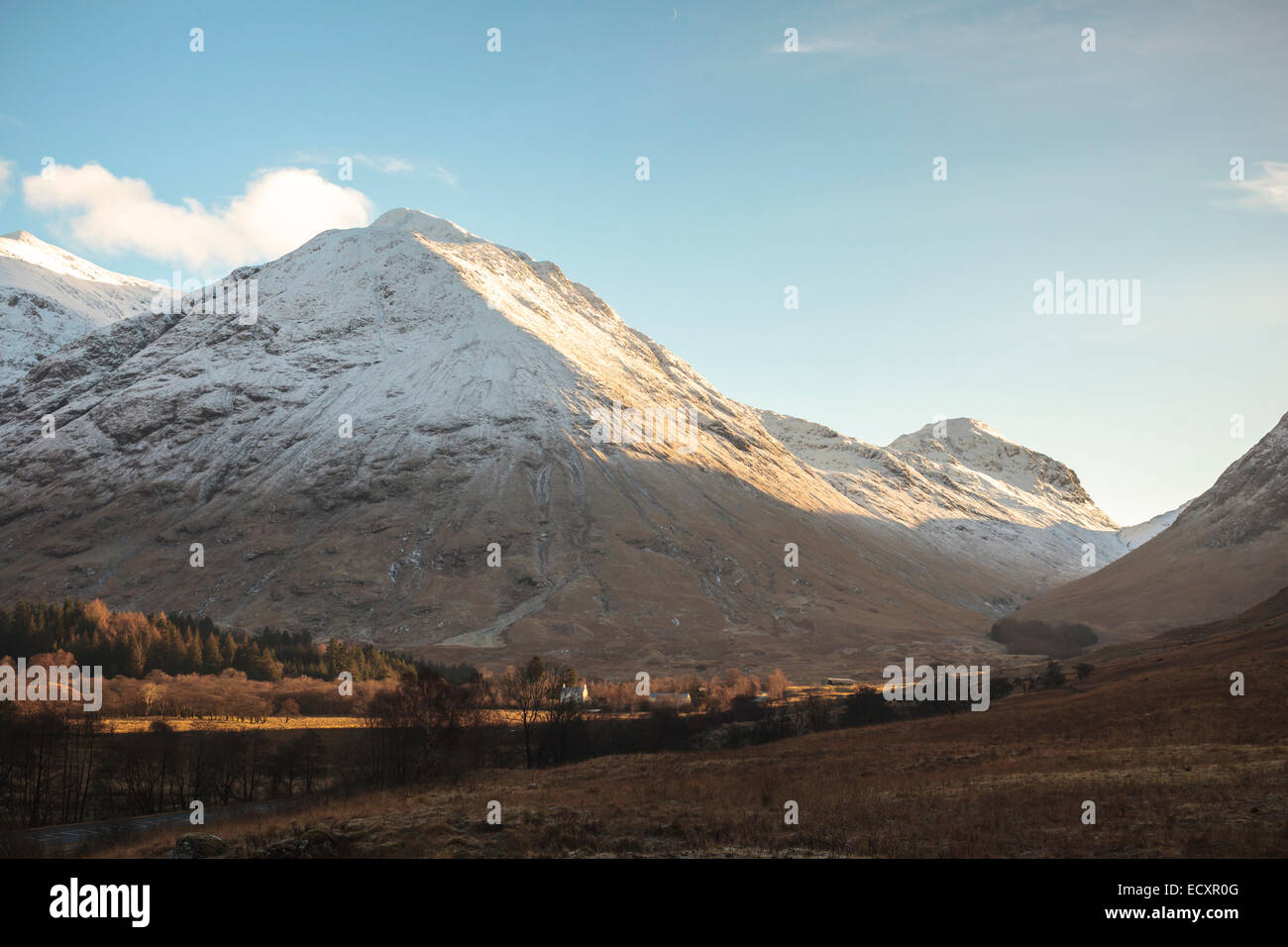 Soleil de l'après-midi sur les sommets volcaniques enneigés de Glen Coe, en Écosse, dans les Highlands écossais. Une ferme est éclairé par la lumière du soleil. Banque D'Images