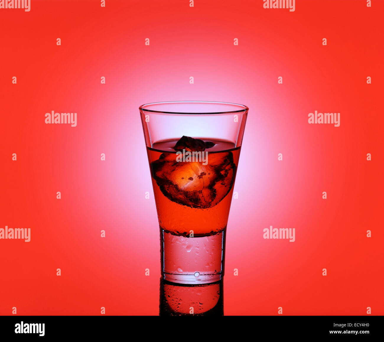 Peu de verre avec un liquide rouge et des cubes de glace, fond rouge Banque D'Images