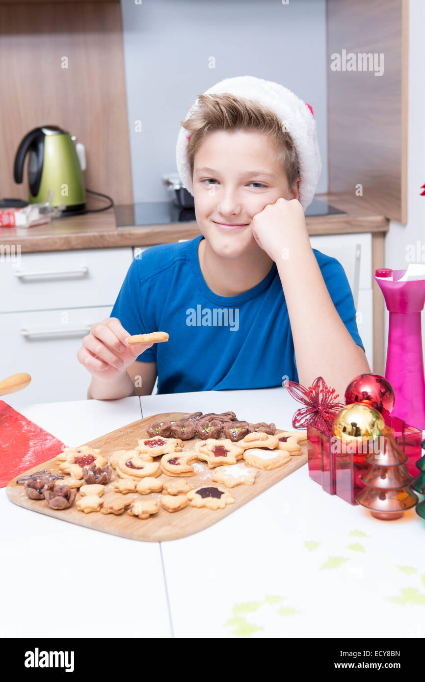 Garçon assis dans la cuisine, manger des petits biscuits de Noël Banque D'Images