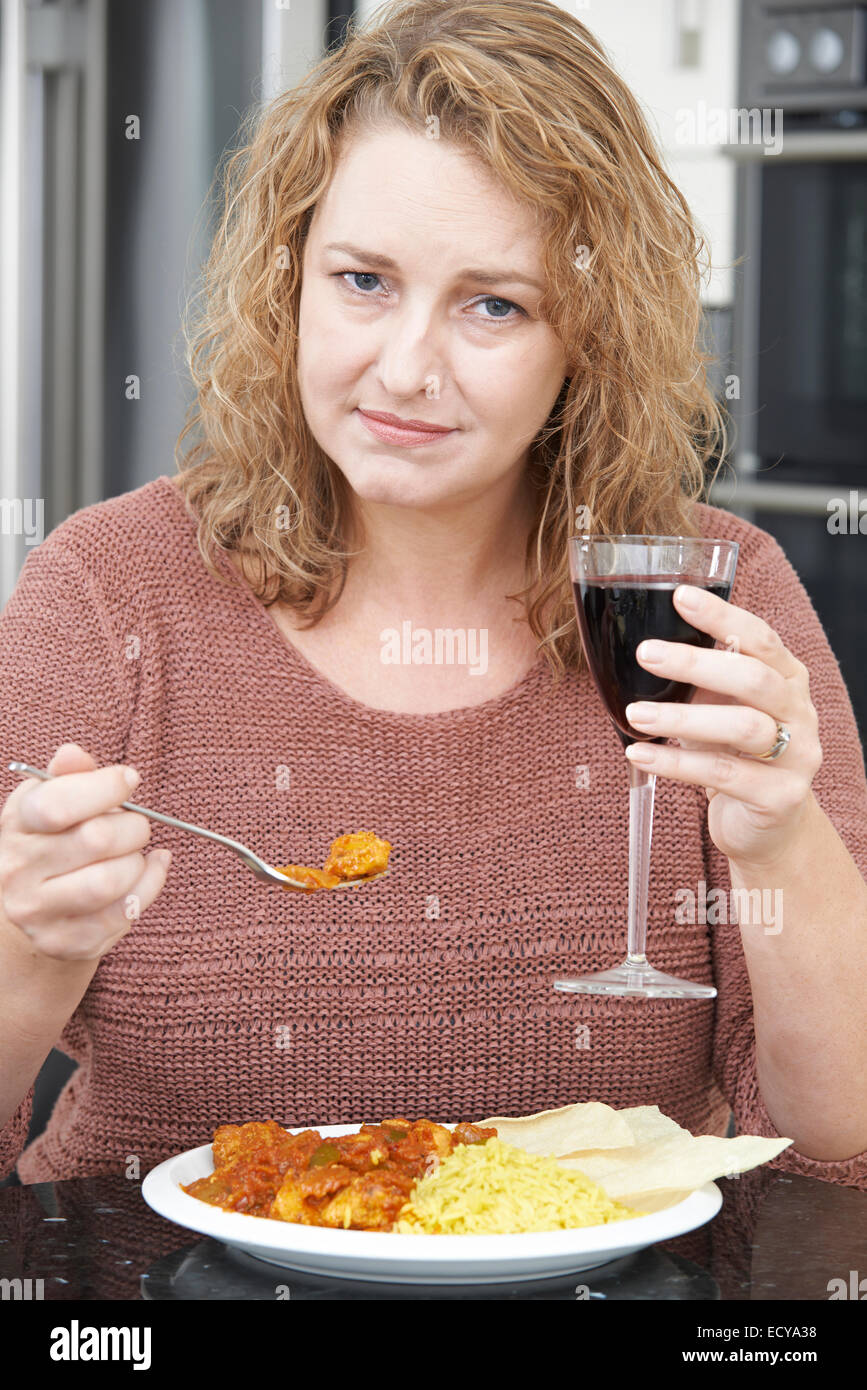 Coupable Woman Eating Curry à emporter et boire du vin Banque D'Images