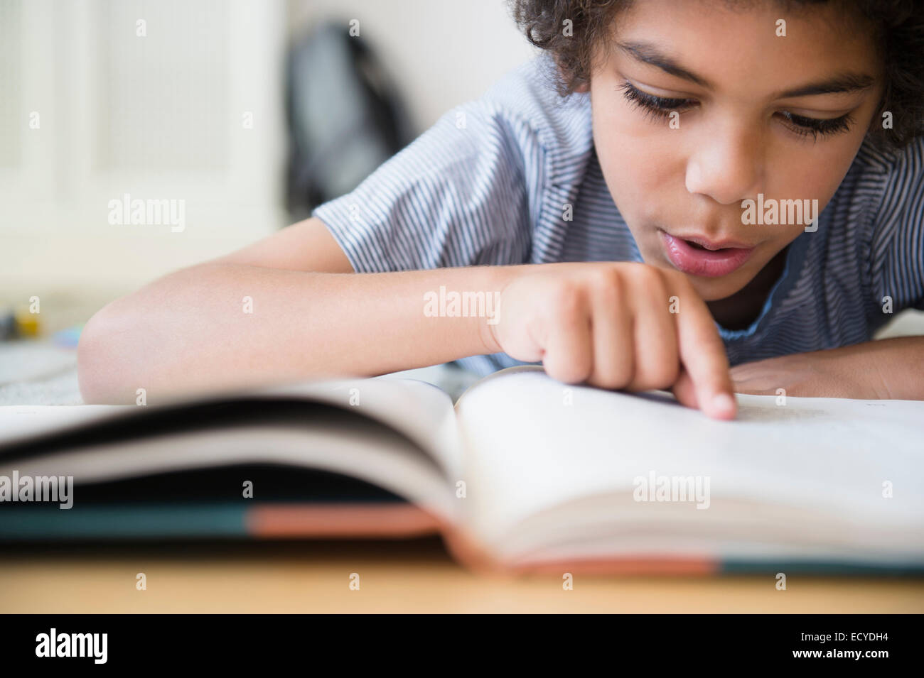 Mixed Race boy reading book at desk Banque D'Images