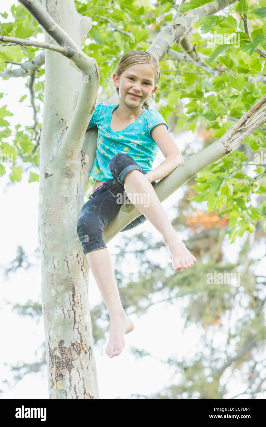 Smiling Caucasian girl climbing tree outdoors Banque D'Images