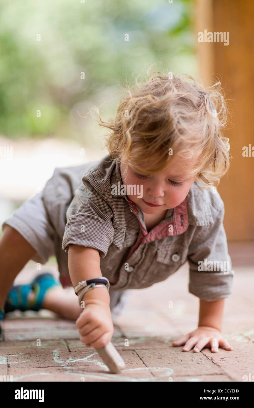 Caucasian baby boy dessin à la craie sur patio en briques Banque D'Images
