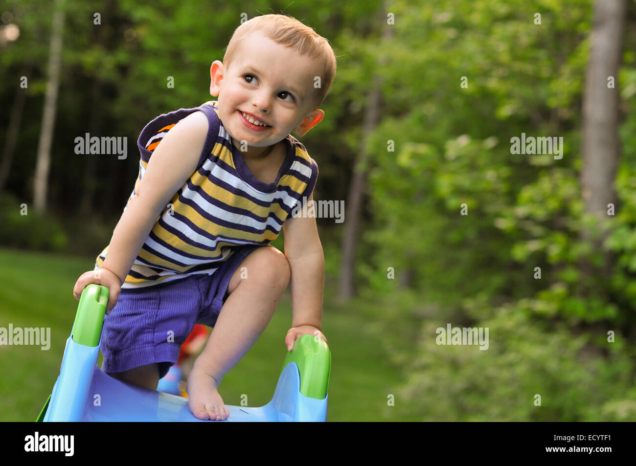 Un bébé garçon dans un débardeur rayé joue sur une glissière en plastique en été. Banque D'Images