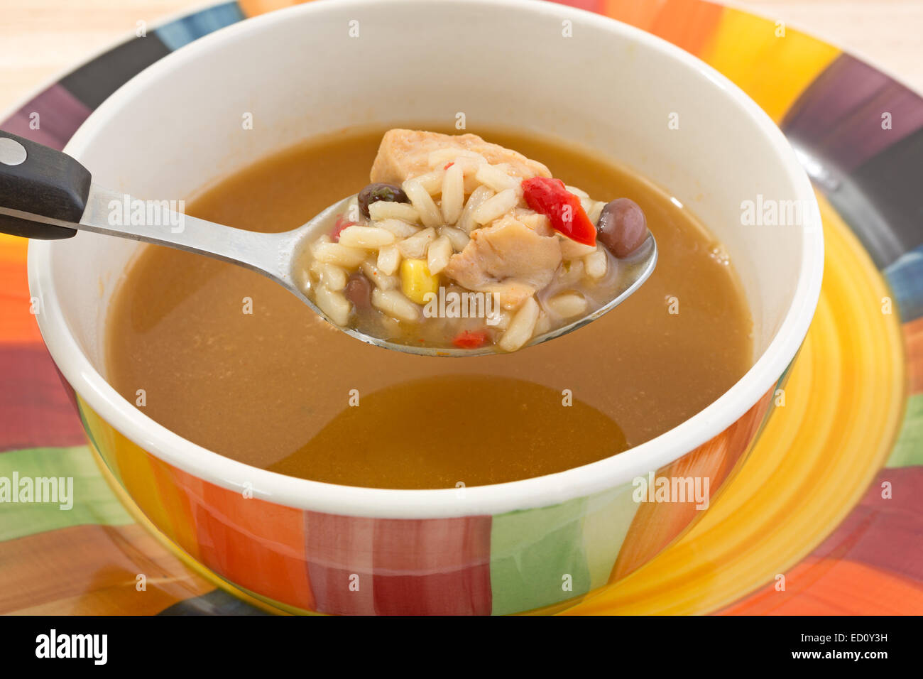 Fermer la vue d'une cuillerée de riz, poulet, poivrons rouges, le maïs et les haricots noirs avec le reste de la soupe dans un bol. Banque D'Images