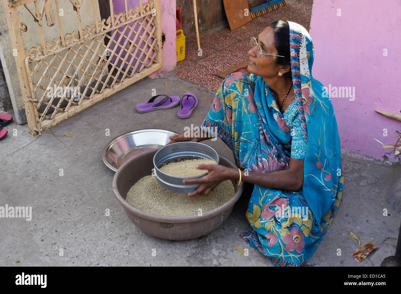 Femme en costume traditionnel grain de tamisage devant sa maison, Patan, Gujarat, Inde Banque D'Images