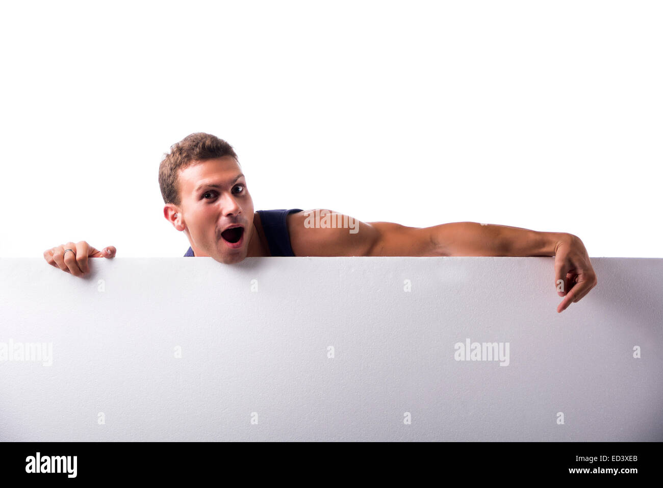 Jeune homme musclé solide derrière une bannière horizontale blanche vierge looking at camera, pointant sur l'copyspace pour votre texte, sur Banque D'Images