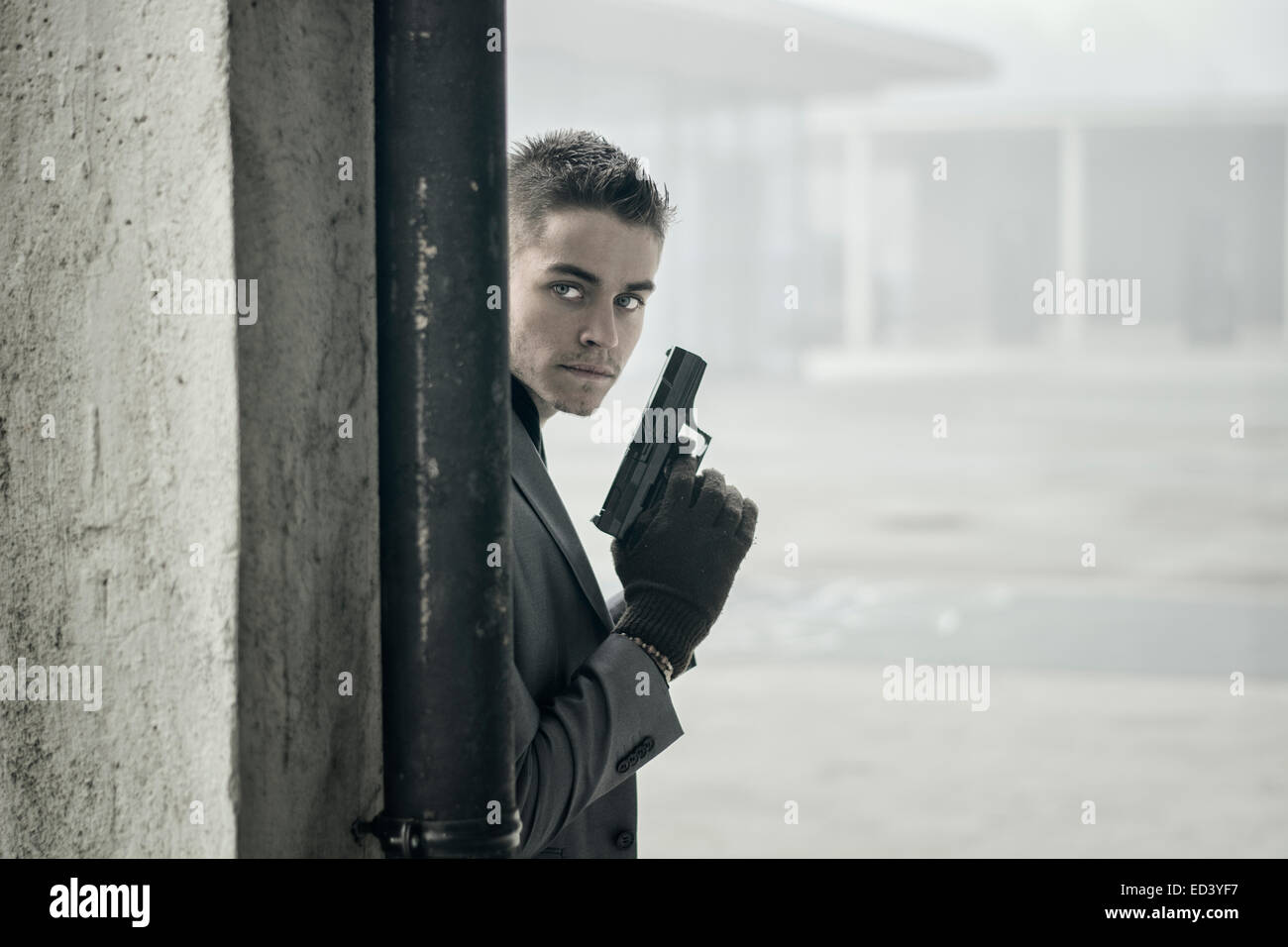 Bien habillé beau jeune détective ou policier ou gangster debout dans un environnement urbain tenant un pistolet avec un déterminé e Banque D'Images