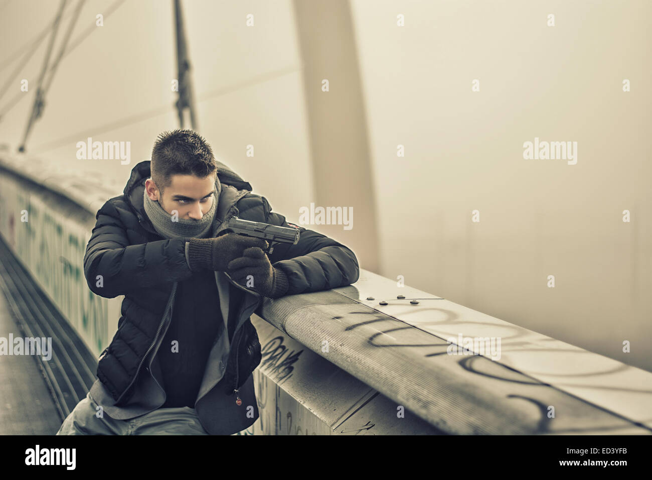 Bien habillé beau jeune détective ou policier ou gangster debout dans un environnement urbain visant une arme à feu à droite Banque D'Images