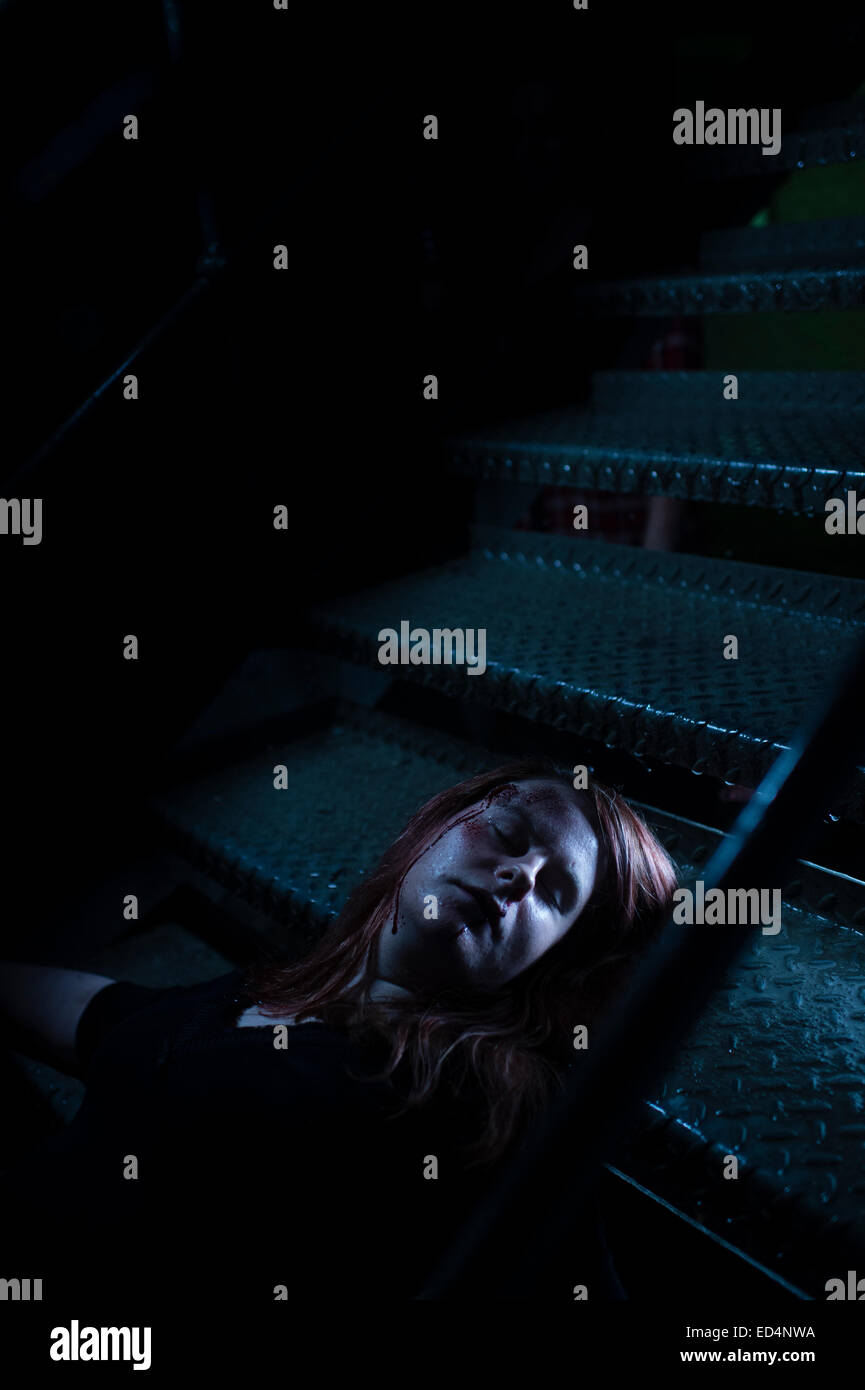Photoshoot : maquillage de fantaisie et les étudiants en design de théâtre jouant un rôle de "meurtre" - une prise de vue girl lying on metal escalier composé de regarder comme si une balle dans la tête, UK Banque D'Images