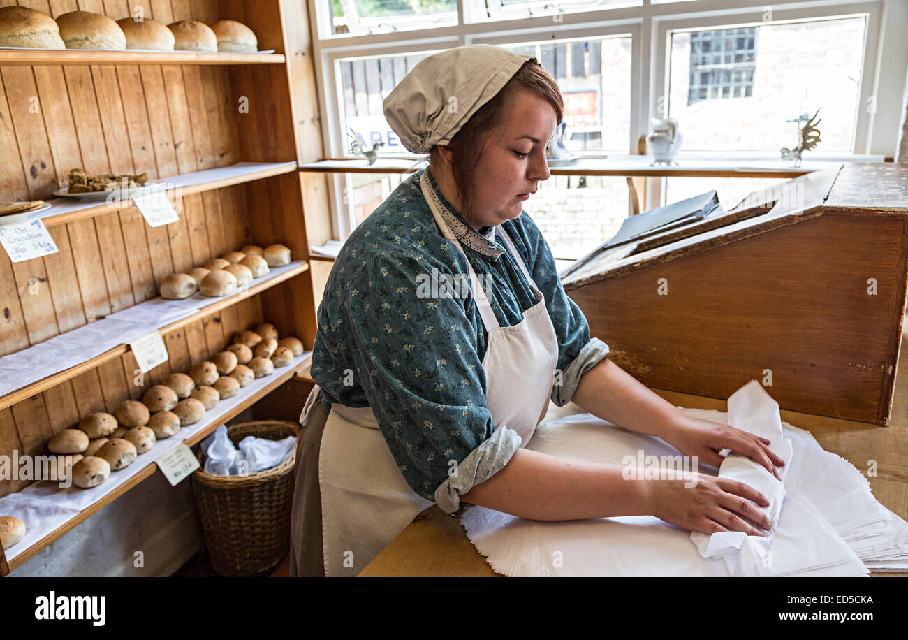 Woman wrapping pain dans du papier pour la vente dans une boulangerie, Blists Hill Victorian town, Ironbridge, Shropshire, England, UK Banque D'Images