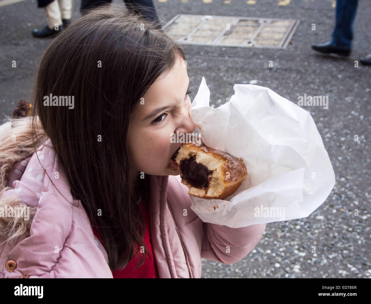 Une jeune fille mange un énorme beignet au chocolat Banque D'Images