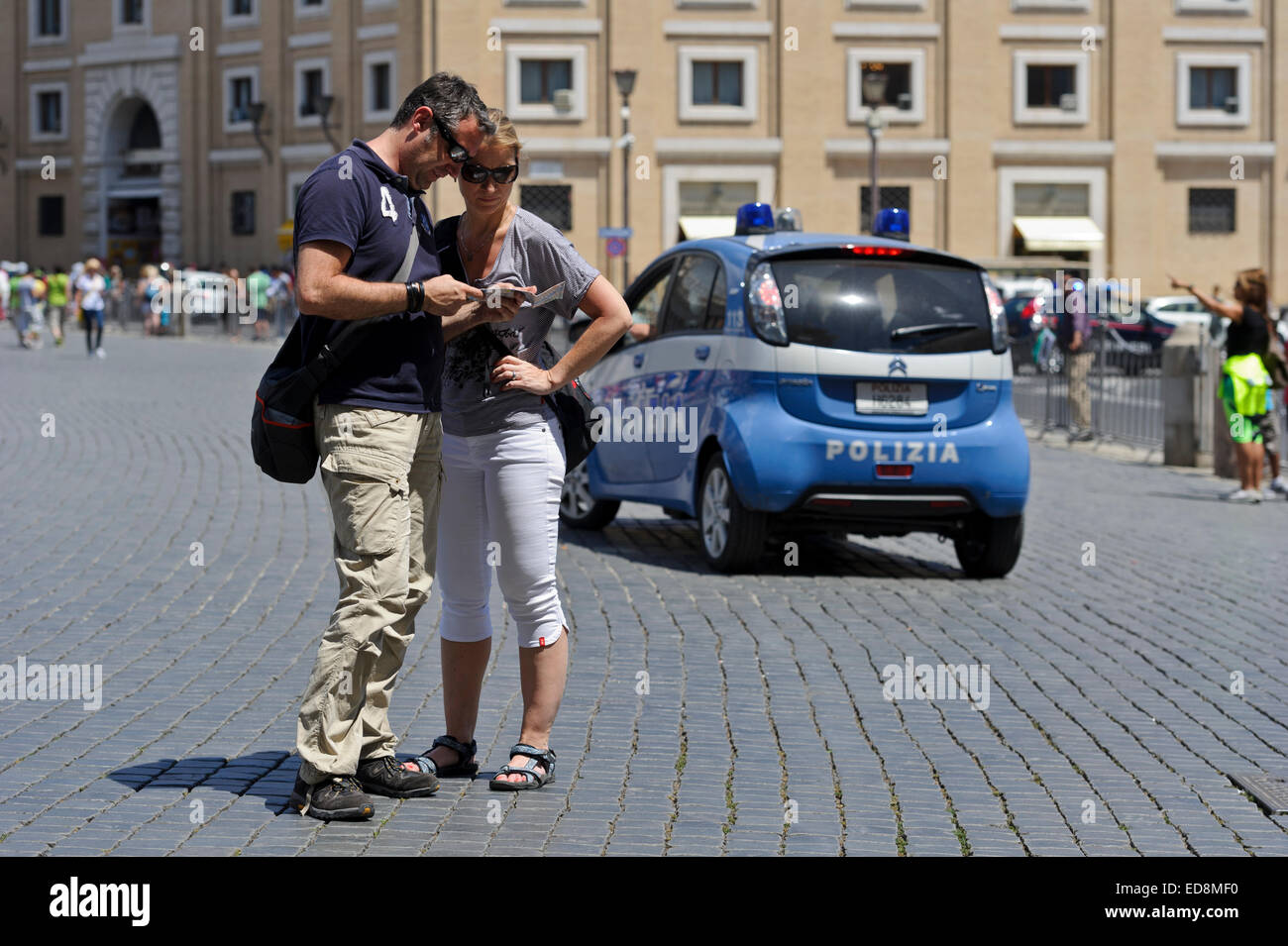 Un couple en regardant une carte dans leurs mains sur la Place Saint-Pierre dans la Cité du Vatican avec une petite voiture de police moderne à l'arrière-plan. Banque D'Images