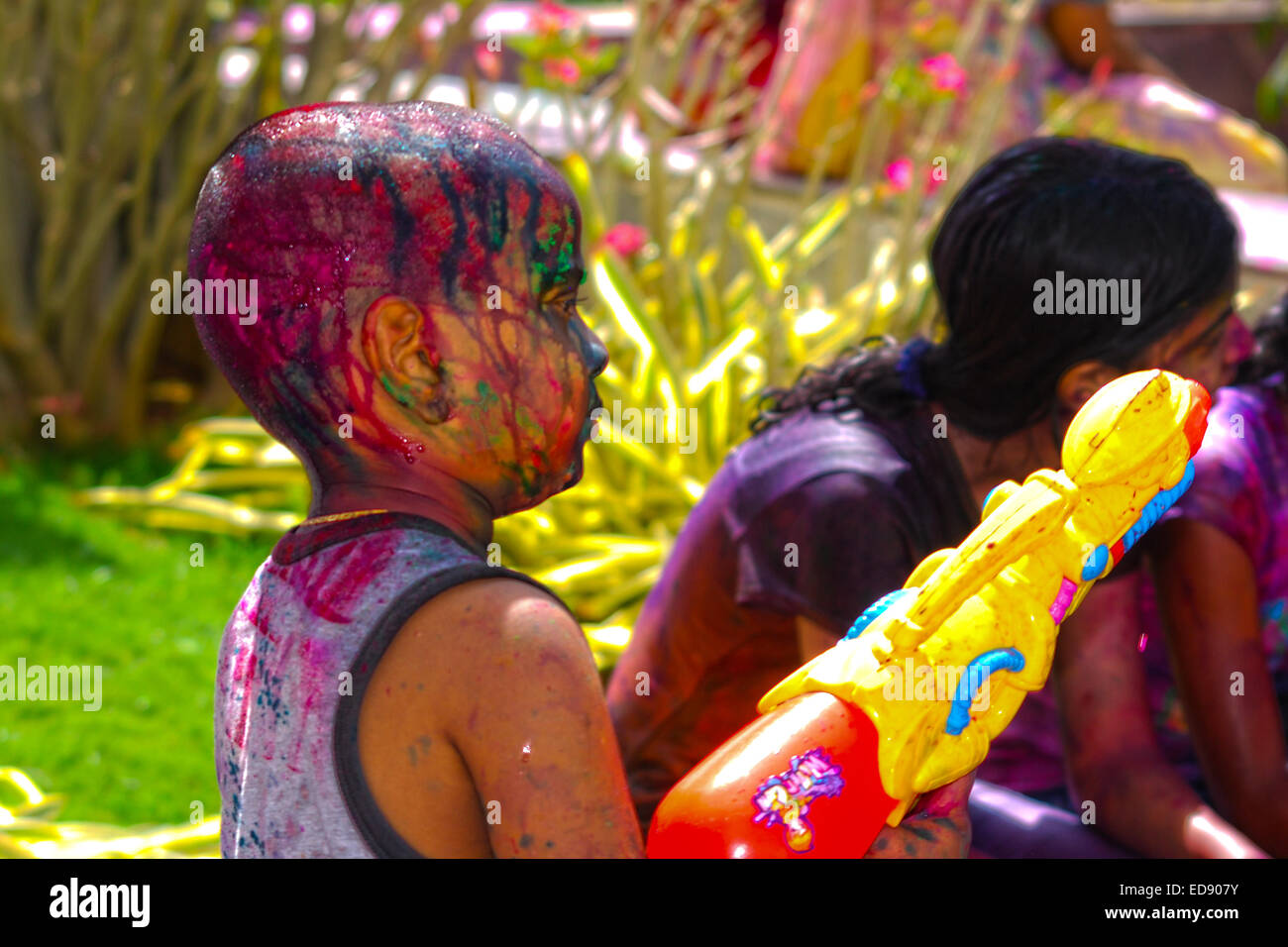 Un jeune garçon indien fait raser la tête couverte de couleurs au printemps fête hindoue holi exerçant également un canon à eau. Banque D'Images