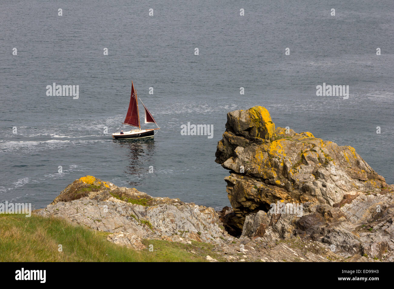 Bateau à voile avec un voile rouge, sur une mer calme, l'Arrondissement Chaises Rock Station de Sauvetage Padstow Cornwall, UK. Banque D'Images
