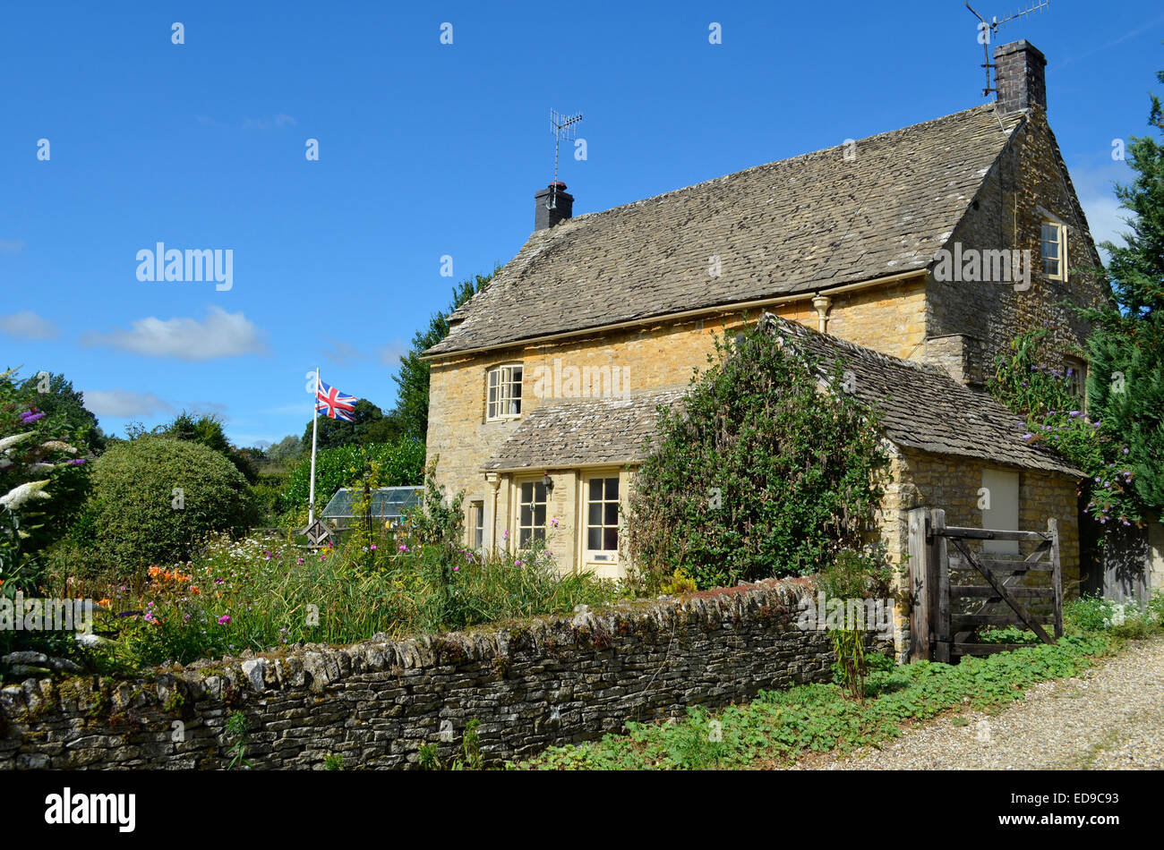Une pierre de Cotswold cottage anglais avec un jardin plein de fleurs et d'un drapeau britannique dans la région de Slaughter, Cotswolds, Royaume-Uni. Banque D'Images