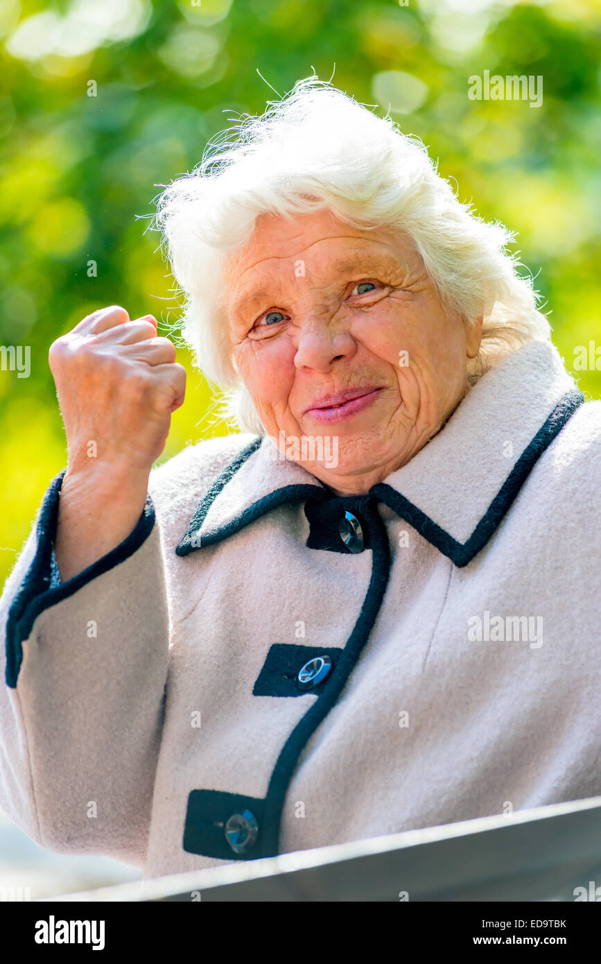 Vieille dame aux cheveux gris montre un poing dans le parc Banque D'Images