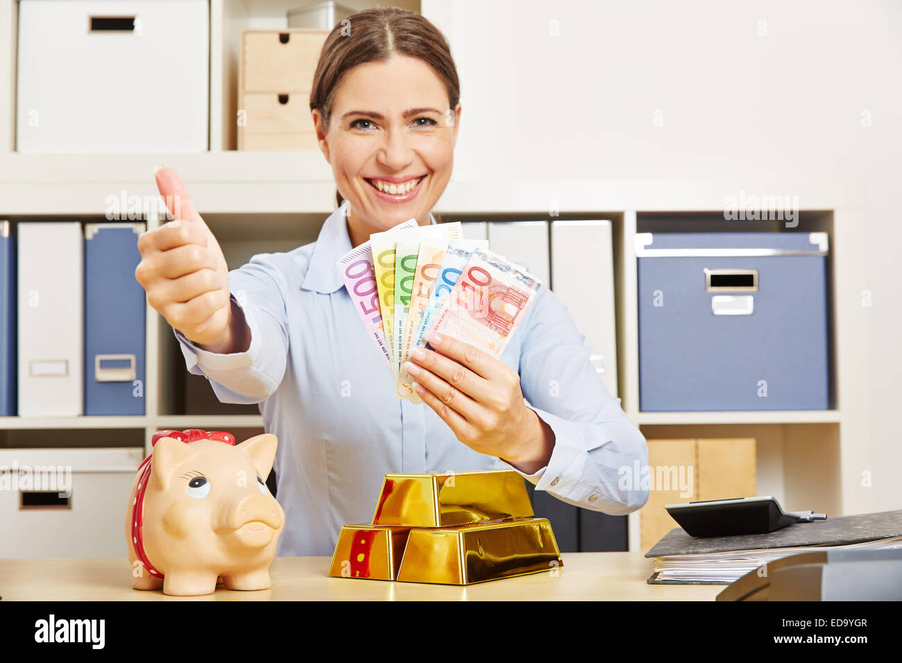 Smiling woman réussie avec de l'argent et or holding her Thumbs up Banque D'Images