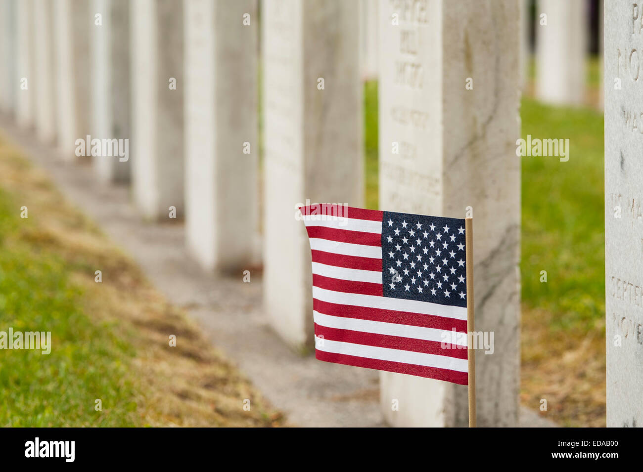 Chef des pierres sur un cimetière sur l'après-midi de printemps avec des pierres tombales en rangs avec un drapeau américain placé à l'une des pierres tombales Banque D'Images