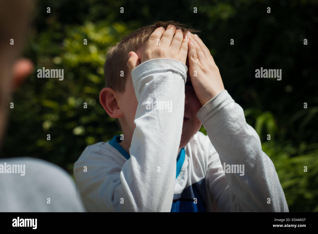 Boy Hiding behind mains tout en jouant à cache-cache Banque D'Images