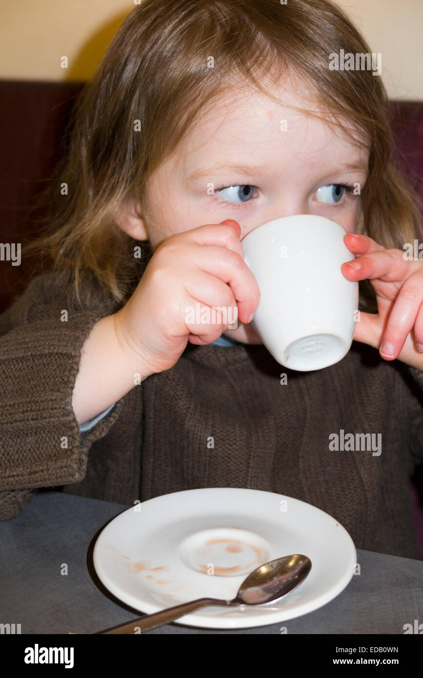 Jeune fille âgée de deux ans / 2 ans s'abreuver à une petite tasse et soucoupe () de babyccino cinno bébé dans un café / restaurant. Banque D'Images