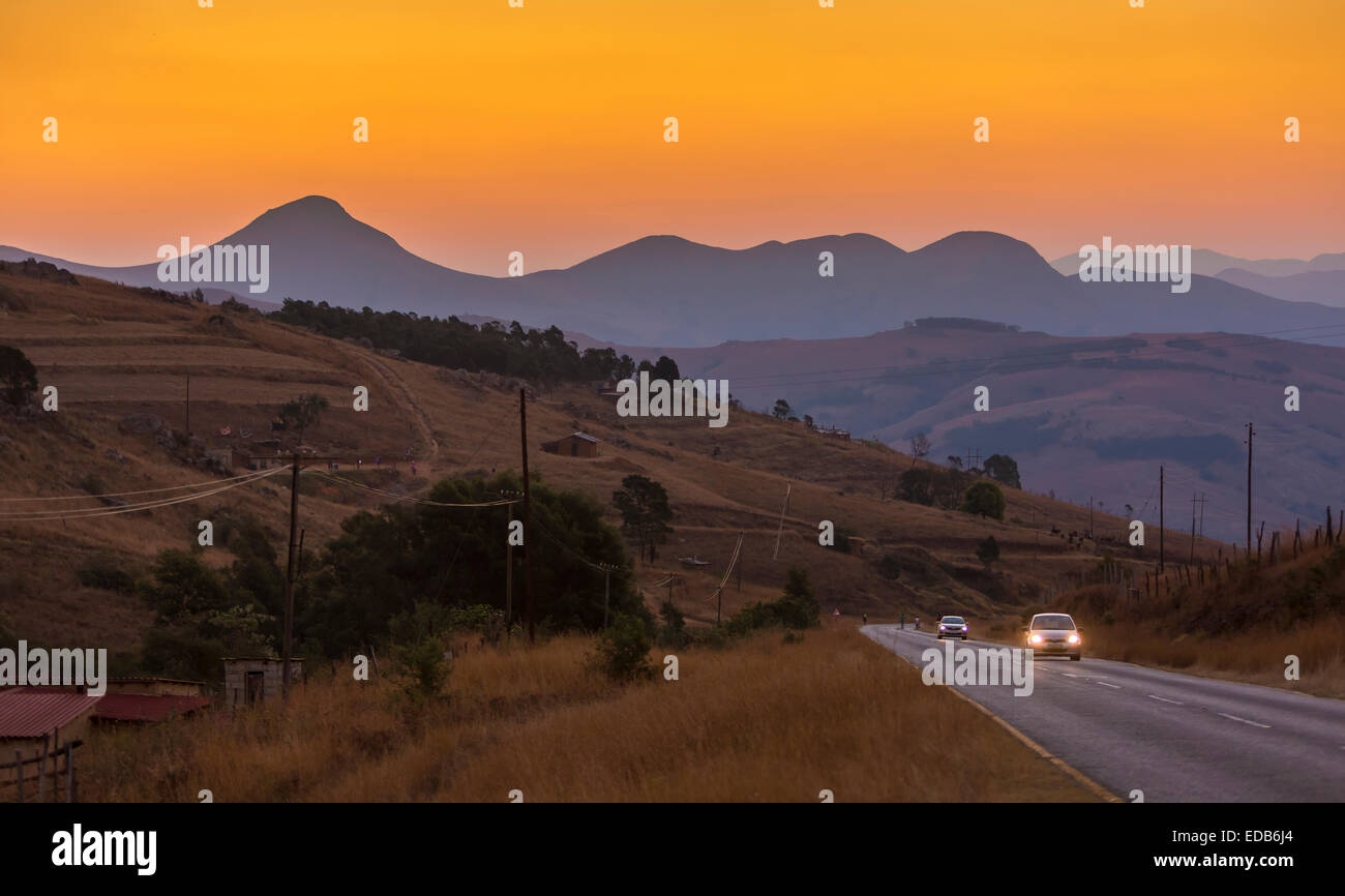 SWAZILAND, Afrique - la fumée de feu de bois d'orange crée coucher de soleil sur paysage de montagnes, comme les voitures roulent sur l'autoroute. Banque D'Images