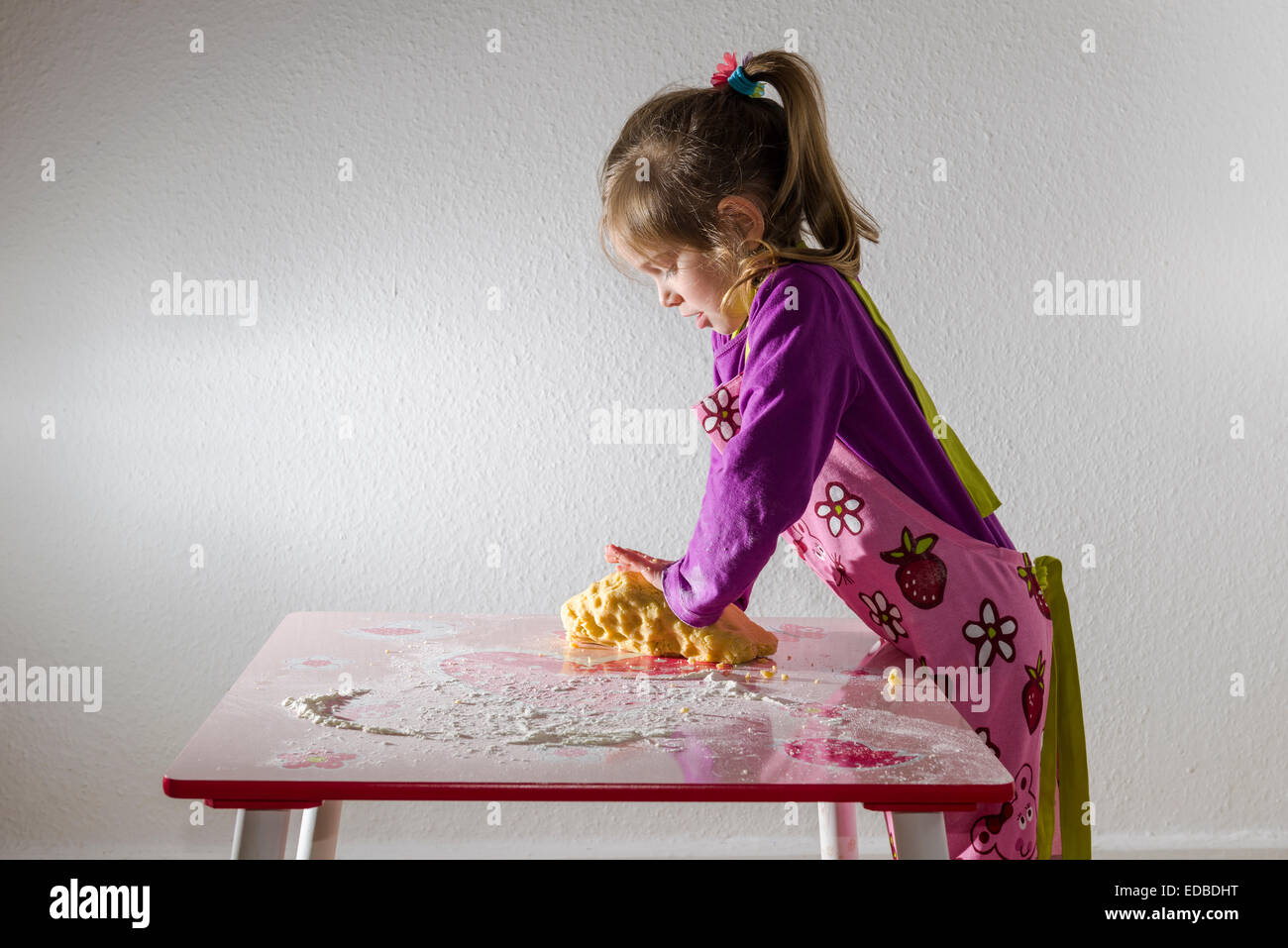 Fille, 3 ans, la levure, pétrir un morceau de pâte sur une table Banque D'Images