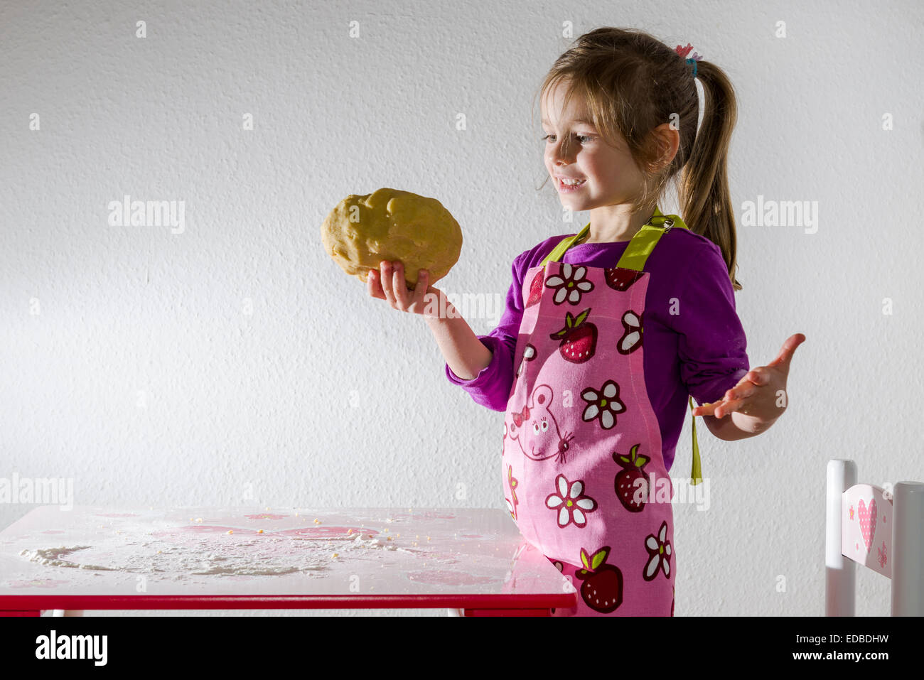 Fille, 3 ans, la cuisson, tenant un morceau de pâte dans sa main Banque D'Images
