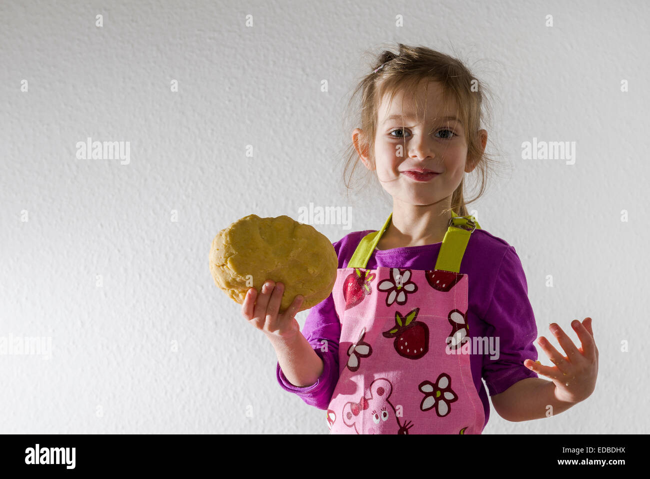 Fille, 3 ans, la cuisson, tenant un morceau de pâte dans sa main Banque D'Images