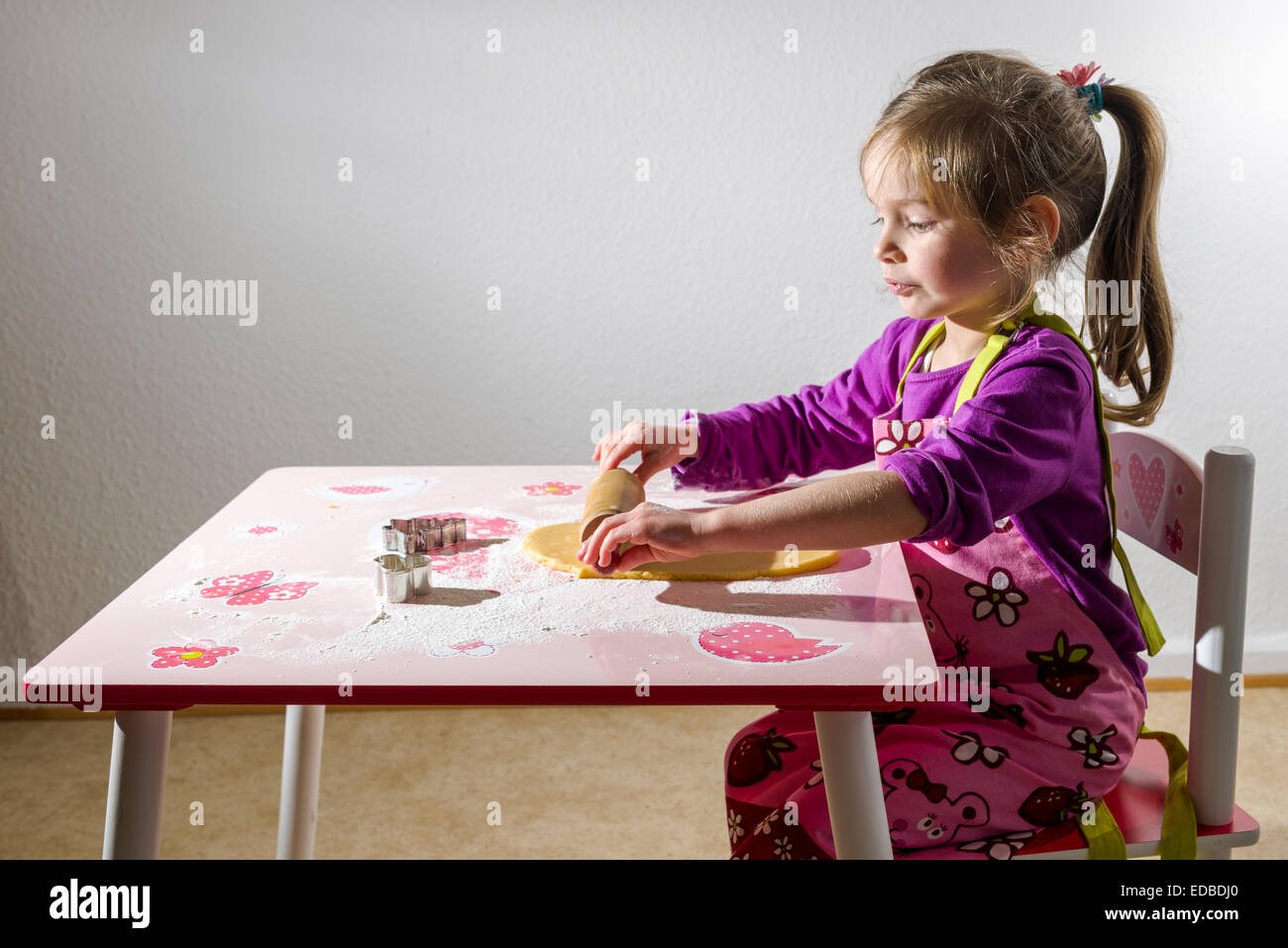 Fille, 3 ans, baking Christmas Cookies, rouler la pâte sur une table Banque D'Images