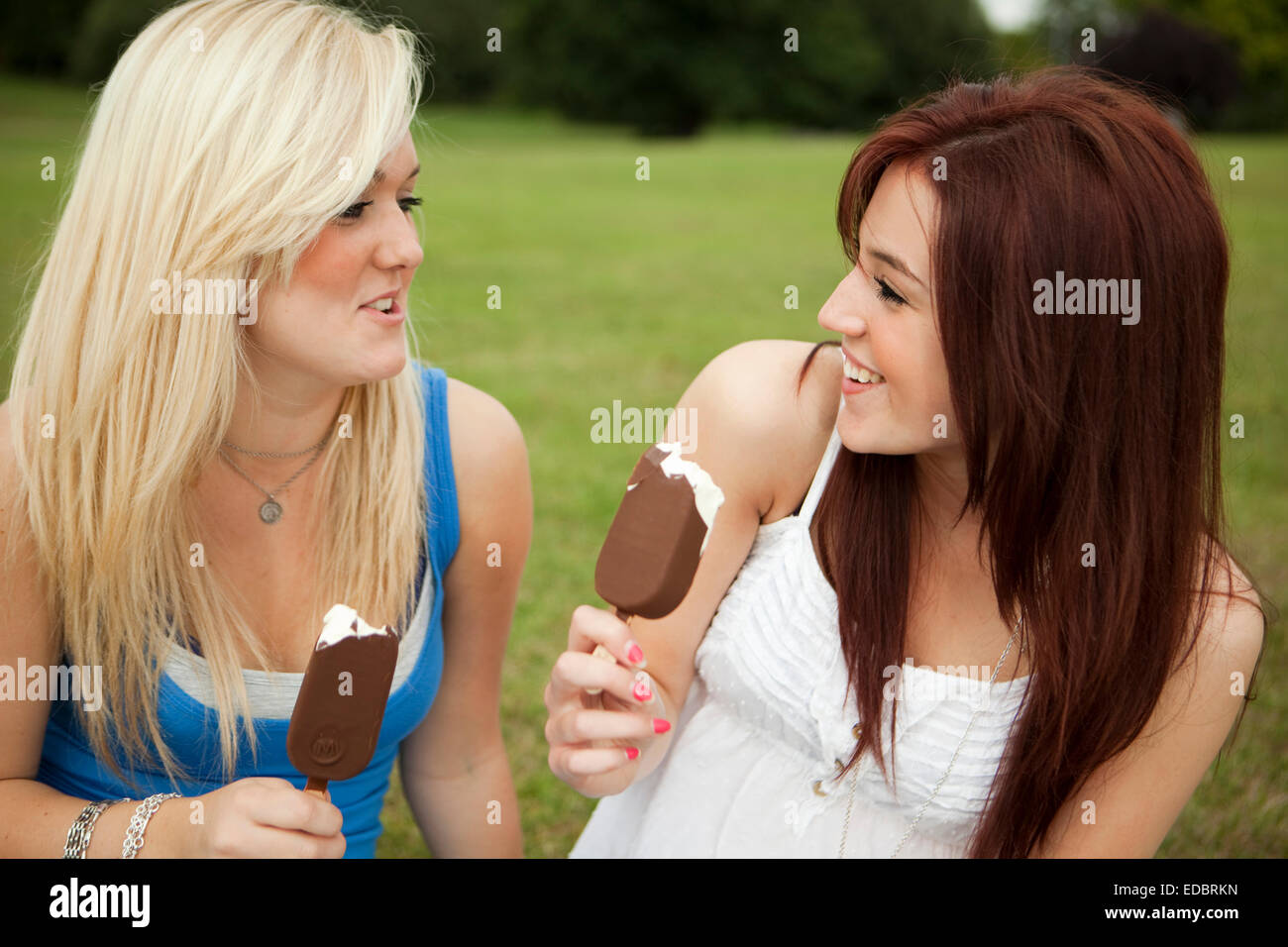 Deux jeunes filles se détendre dans le parc, bénéficiant d'une des glaces Magnum. Banque D'Images