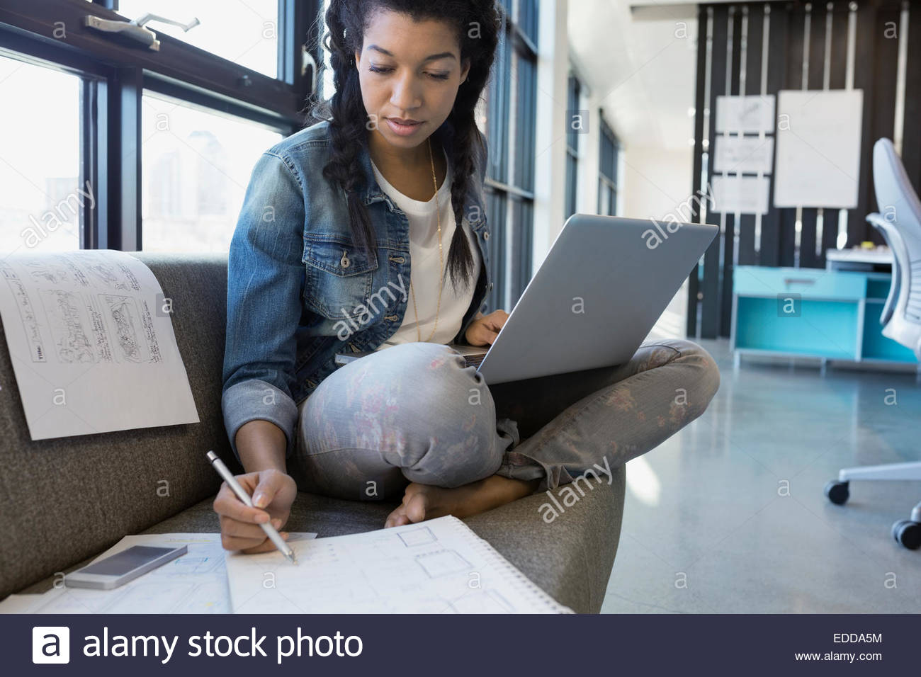 Designer working at laptop on sofa in office Banque D'Images