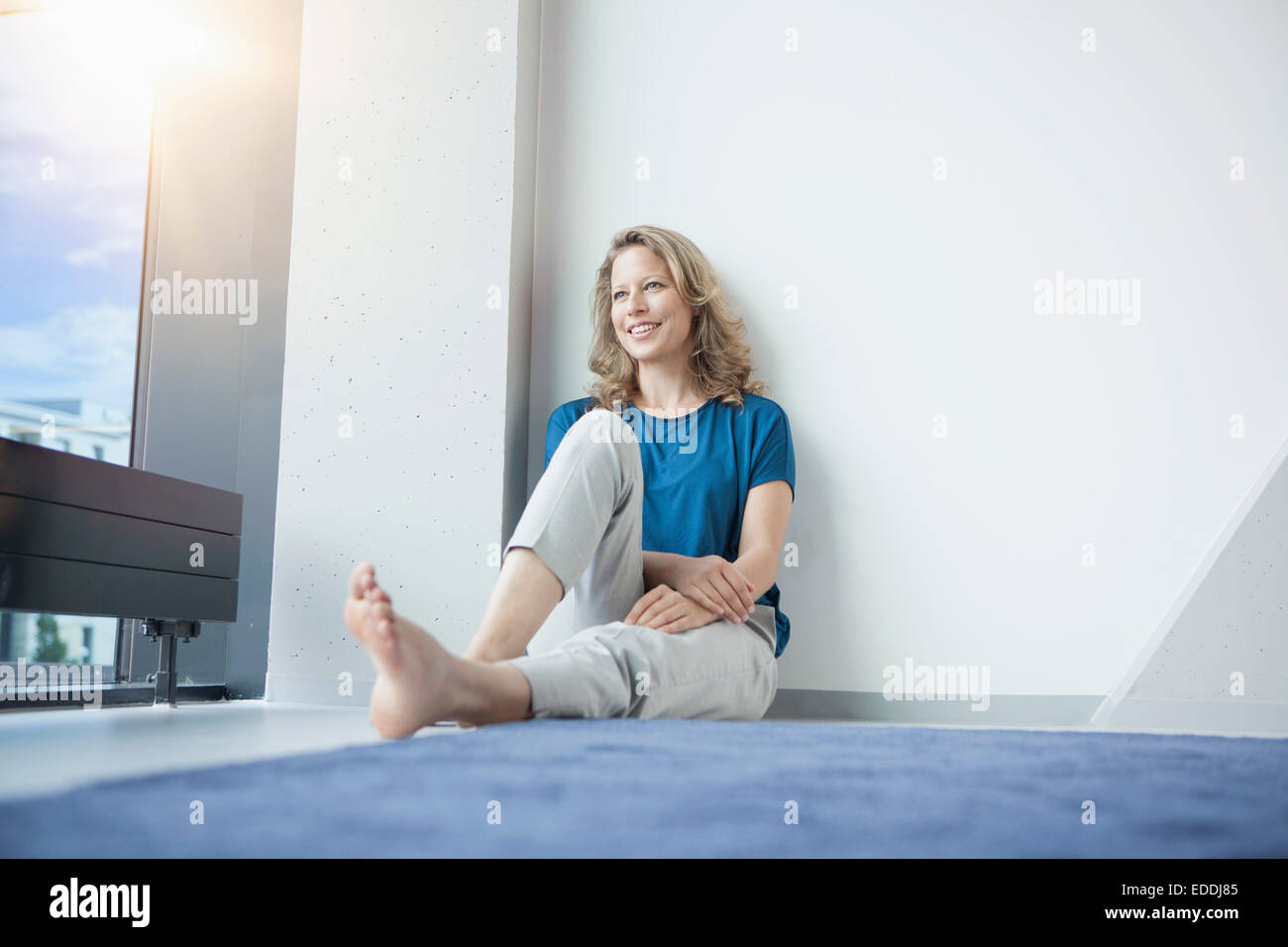 Portrait of smiling mature woman sitting sur le sol dans son appartement Banque D'Images