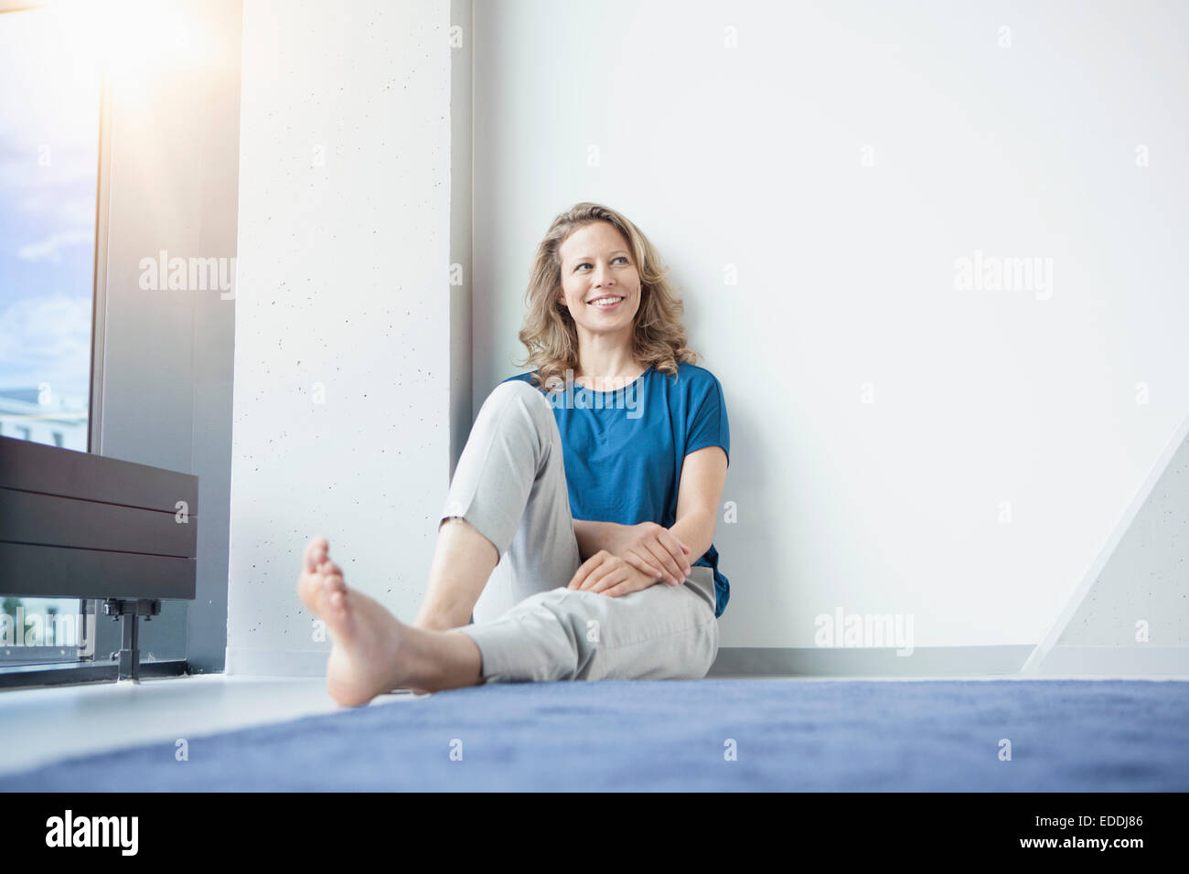 Portrait of smiling mature woman sitting sur le sol dans son appartement Banque D'Images