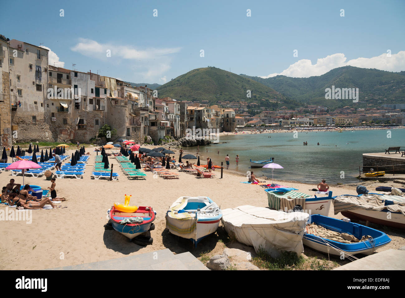Les humains et les bateaux sur la plage du vieux port et de la vieille ville de Cefalu Sicile Italie avec de vieux bâtiments anciens dans l'arrière-plan. Banque D'Images