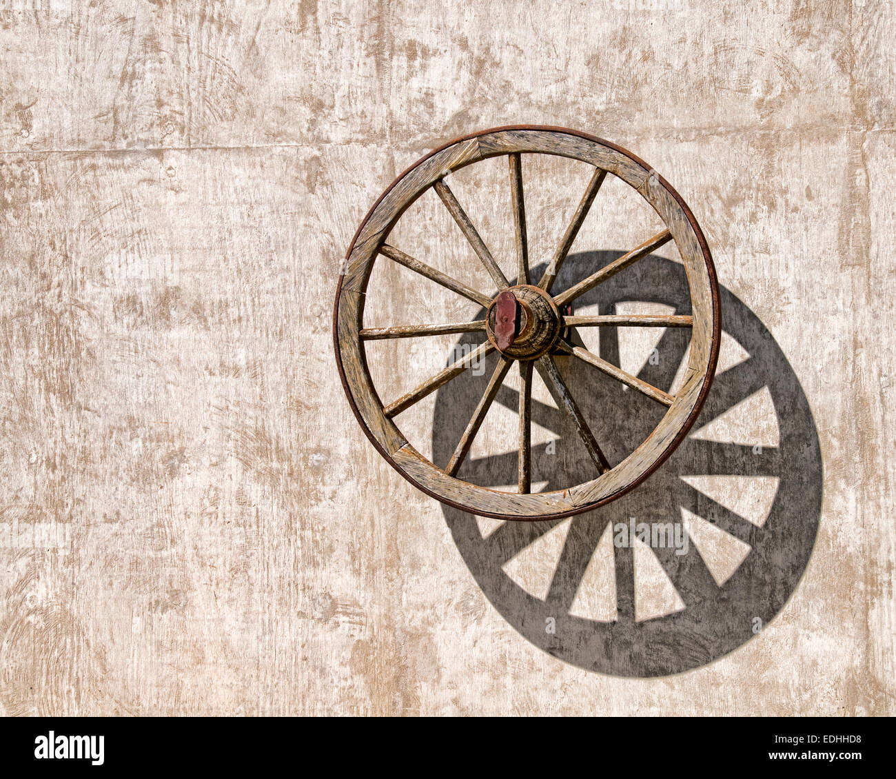 Une vieille roue de chariot en bois jette une ombre sur un mur de béton Banque D'Images