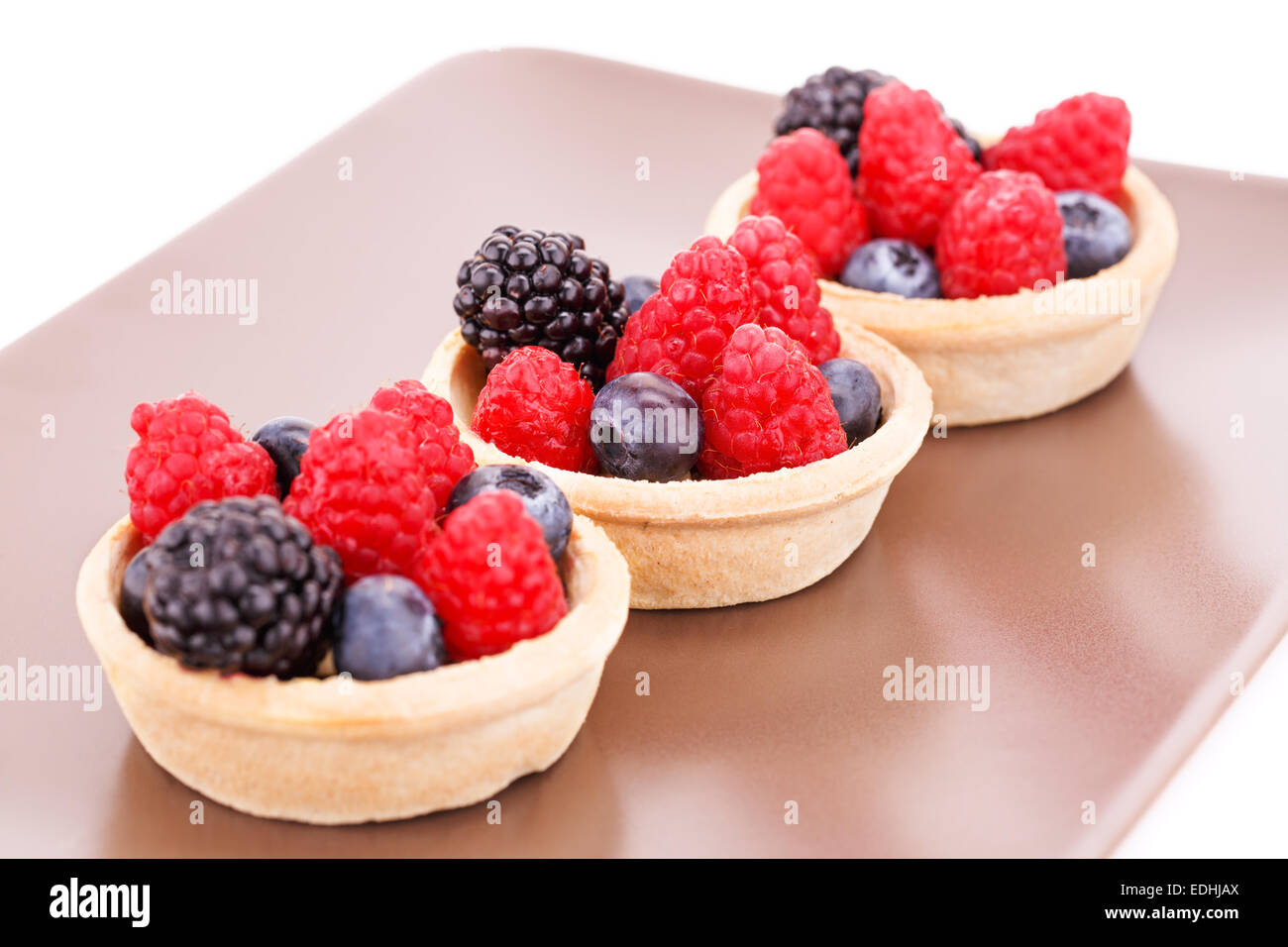 Tartelettes aux fruits frais mûrs dans sur la plaque brune. Banque D'Images